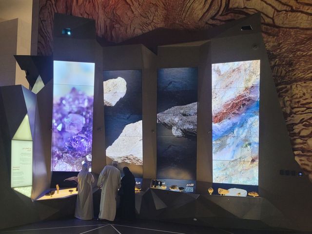 Une exposition composée d'écrans grand format présente des structures minérales et des formations géologiques. Les visiteurs peuvent admirer les pièces exposées dans une salle d'exposition au design moderne.