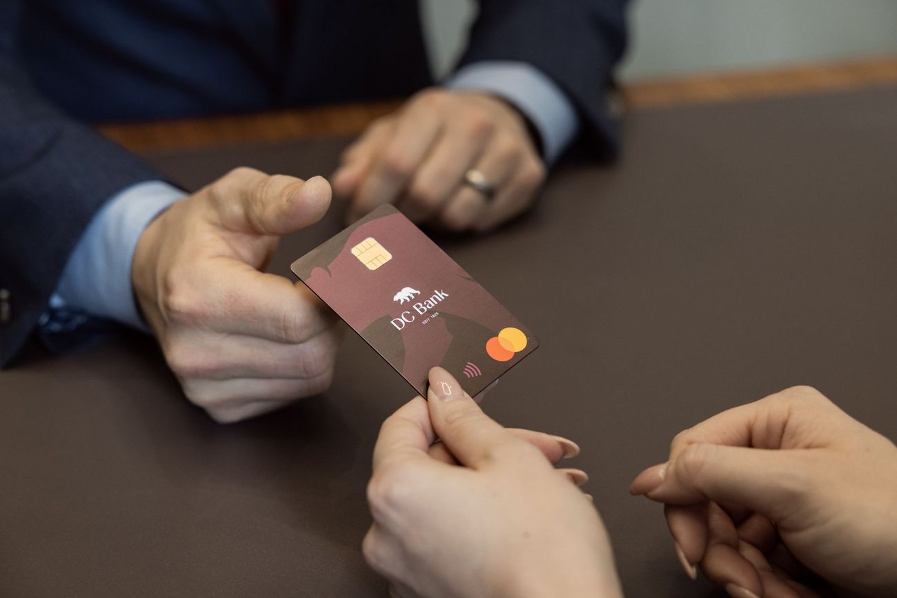 Eine Person übergibt die DC Bank Karte einer anderen Person.