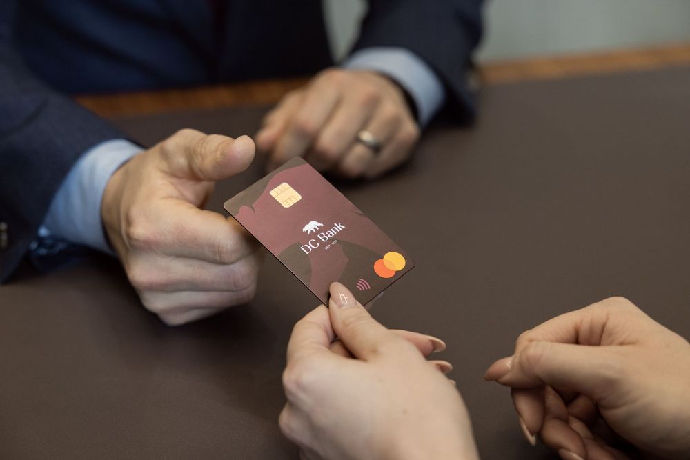 Eine Person übergibt die DC Bank Karte einer anderen Person.