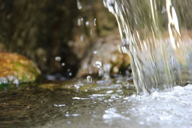 „Nahaufnahme von fliessendem Wasser, das über Steine spritzt.