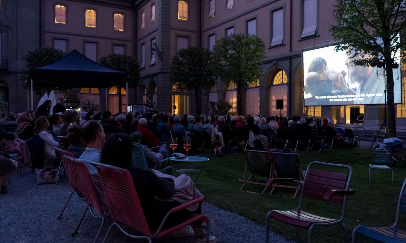 Openair-Kino mit sitzendem Publikum im abendlichen Innenhof.