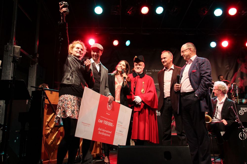 Gruppe von Menschen steht auf einer Bühne und hält einen grossen Spendenscheck über 100’000 CHF.