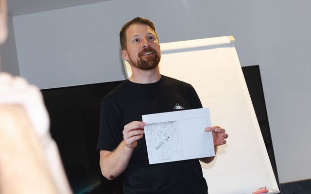 Eine Person steht vor einem Flipchart und präsentiert eine Skizze auf einem Blatt Papier. Die Szene zeigt eine kreative Vorstellung oder Ideation in einem Workshop- oder Präsentationssetting.