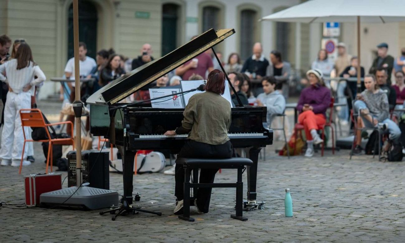 Person spielt Flügel vor sitzendem Publikum im Freien.