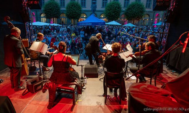 Orchester spielt auf Bühne vor grossem Publikum im Innenhof.
