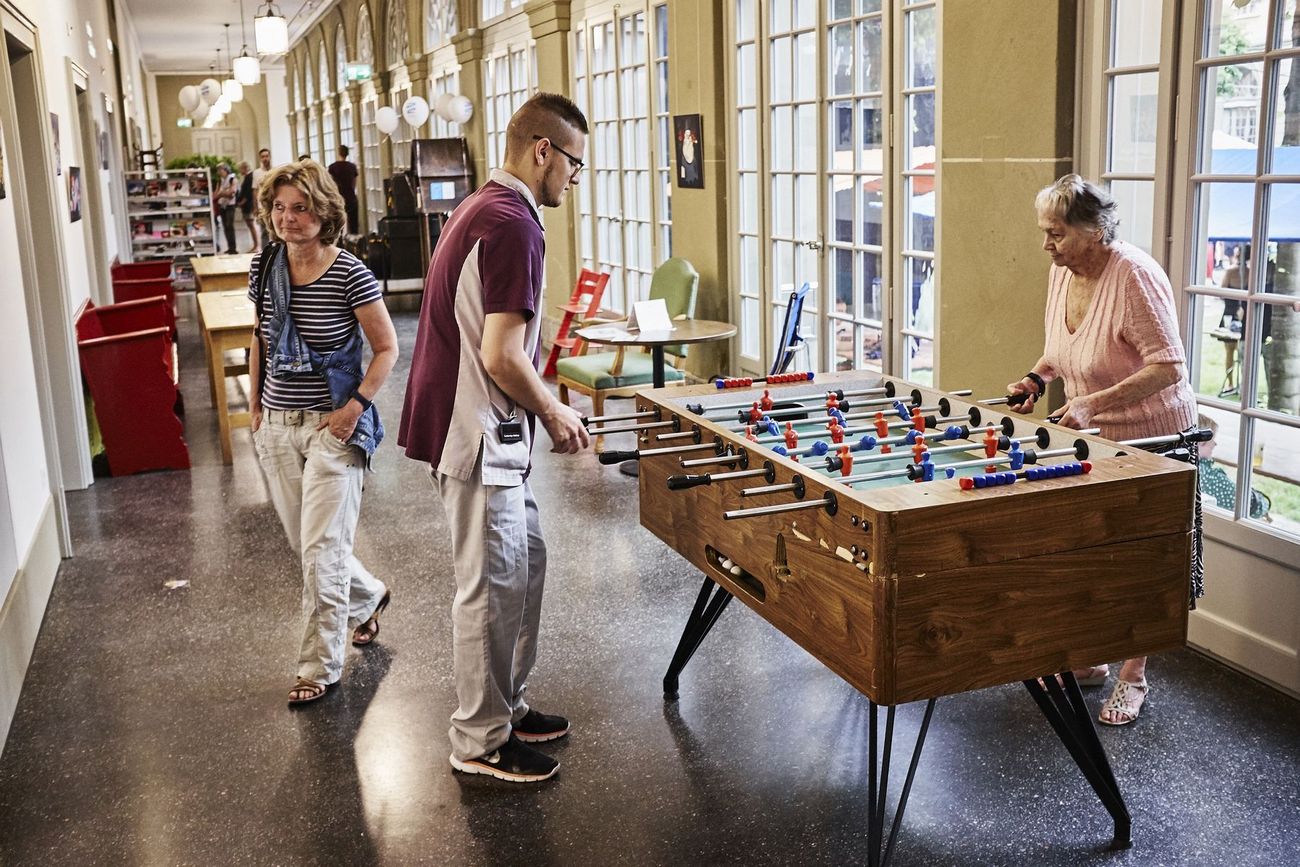 Mehrere Personen spielen und beobachten ein Tischfussballspiel in den hellen Gängen des Berner Generationenhauses.