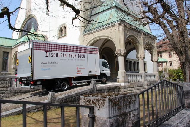Ein Lieferwagen von Tischlein deck dich steht vor einem historischen Gebäude mit Bogengang