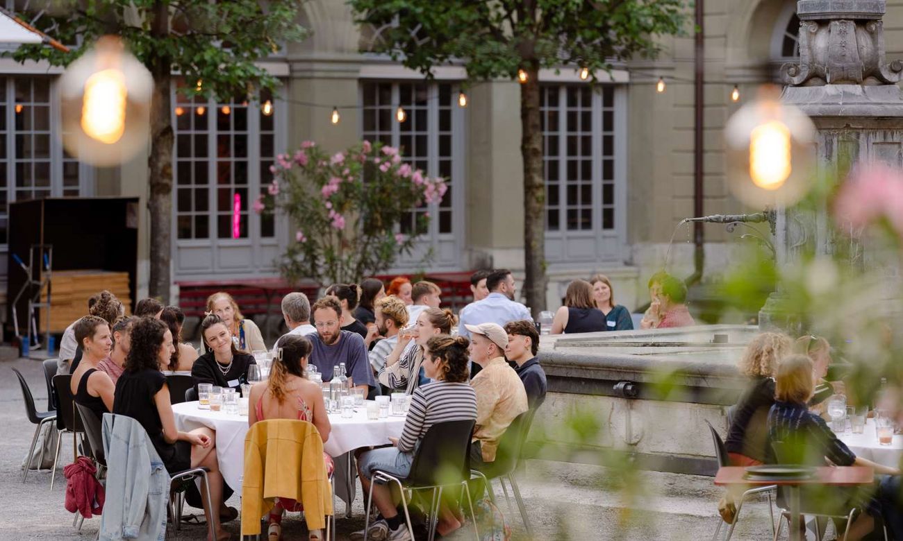 Menschen sitzen bei Kerzenlicht an gedeckten Tischen im Innenhof.