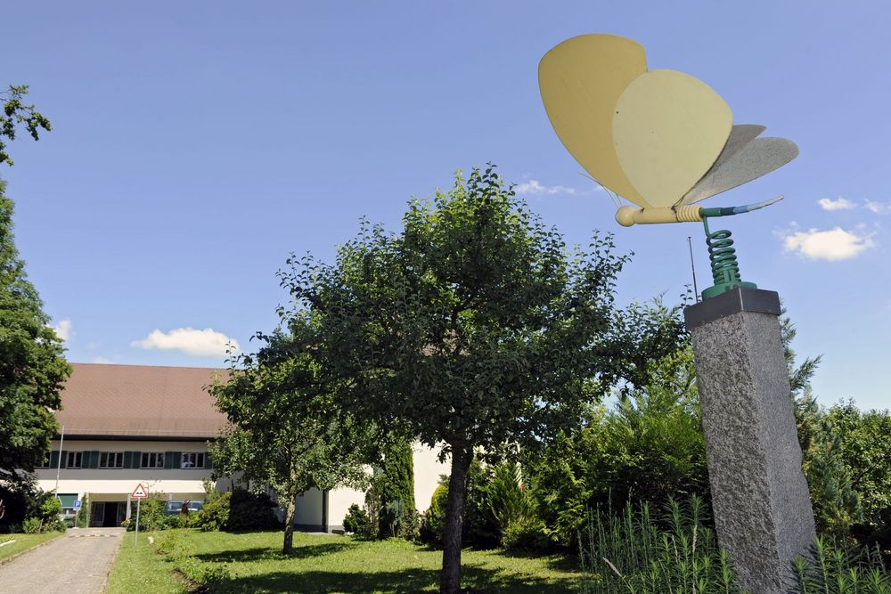 Grosse bunte Schmetterlingsfigur auf einem Pfeiler neben Bäumen.