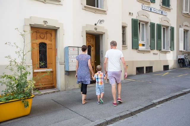 Eltern haben Kind an der Hand und spazieren eine Strasse entlang