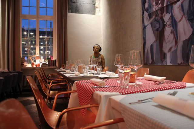 Gemütlich gedeckter Restauranttisch in einem warm beleuchteten Raum, neben einem grossen Fenster mit Abendblick auf den Bahnhofplatz.