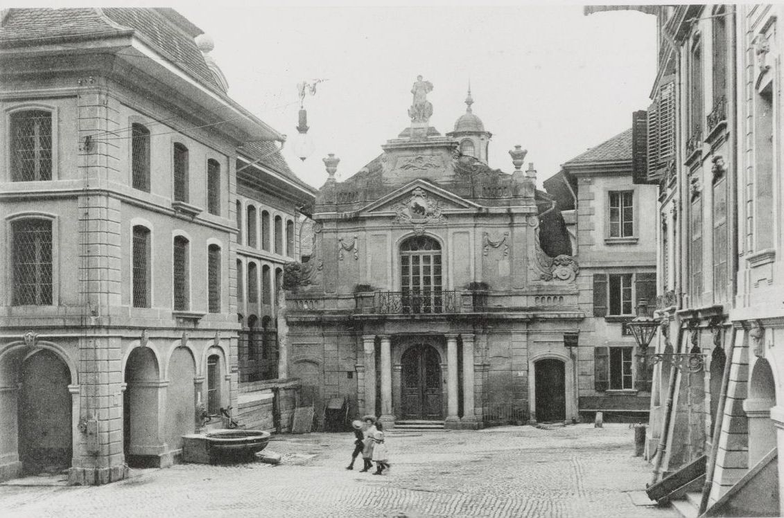 Schwarz-weiss Bild aus einer Strasse mit Altstadtgebäuden links, rechts und im Hintergrund