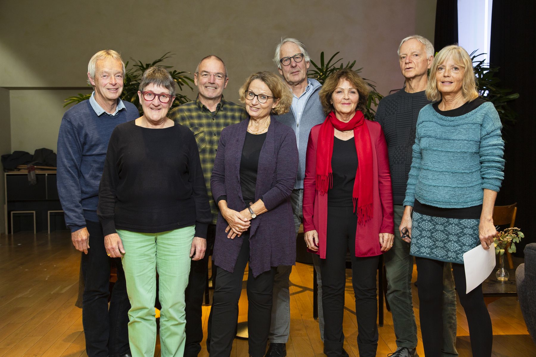 Zwei Personen sitzen auf Sesseln in einem Gespräch, wobei eine Person gestikulierend etwas erklärt. Die Szene wirkt wie ein vertrautes Beratungsgespräch in einem gemütlichen Raum mit dunklem Vorhang und farbigen Kissen.