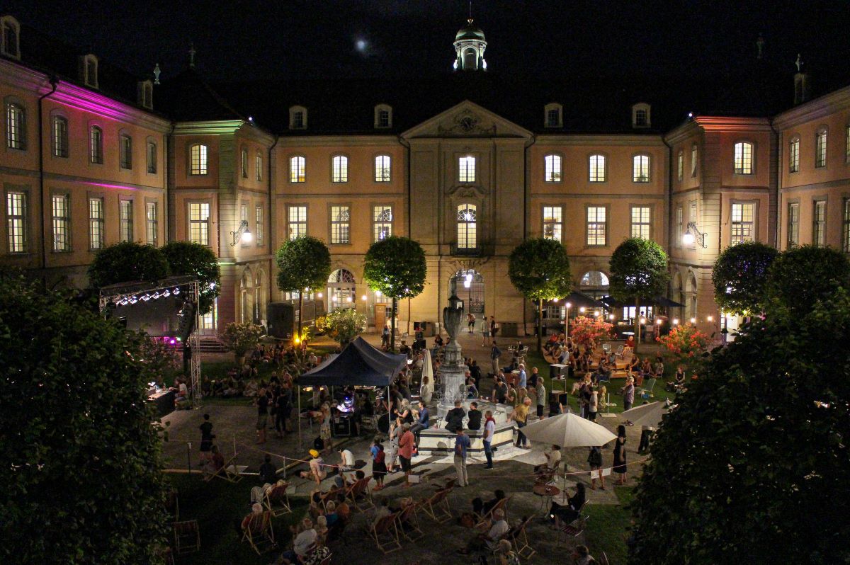 Belebter Innenhof bei Abendveranstaltung mit beleuchtetem Gebäude.