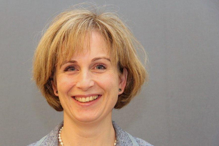 Eine Frau mit kurzem, hellblondem Haar vor neutral grauem Hintergrund