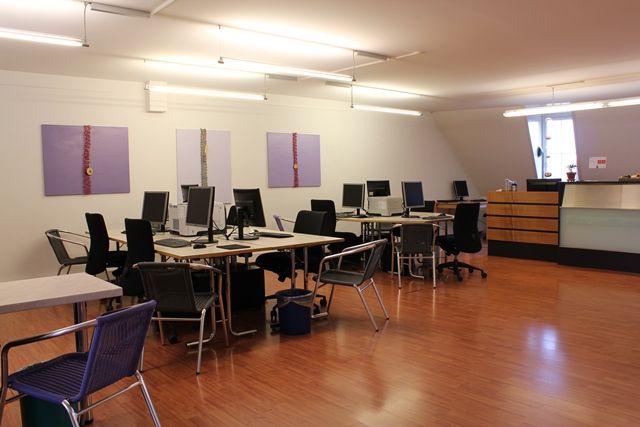 Heller Computerraum mit mehreren Arbeitsplätzen, Schreibtischen und lila Gemälden an der Wand.