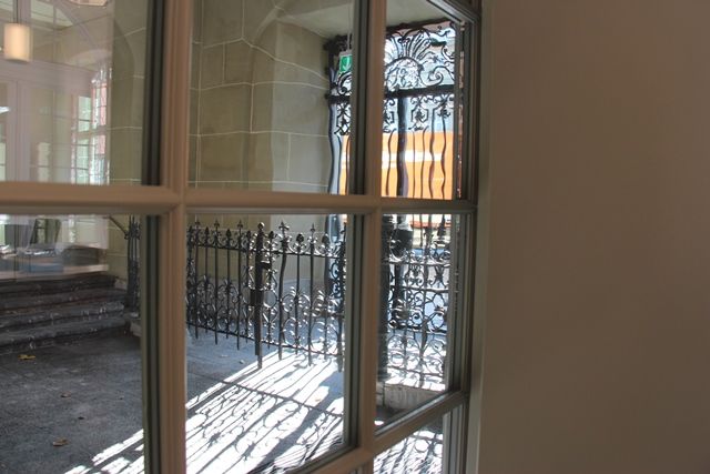 Blick durch ein Fenster auf den Haupteingang des Burgerspitals mit verziertem Eisenportal und Steinbogen.