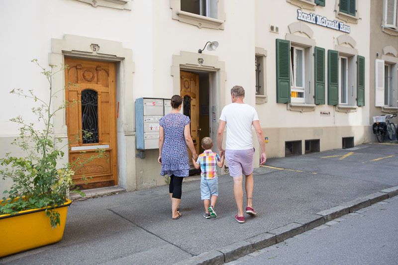 Eltern haben Kind an der Hand und spazieren eine Strasse entlang
